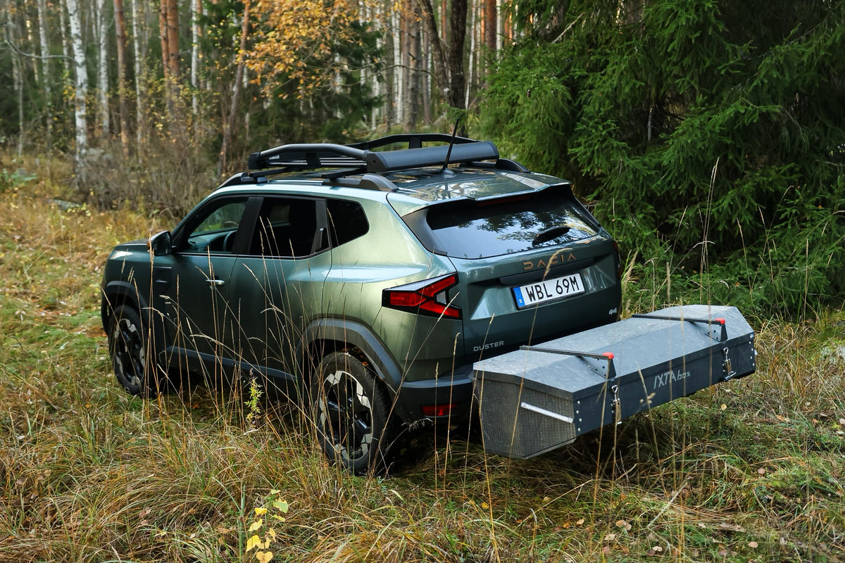Dacia Duster med en monteret IXTAbox bagageboks til anhængertræk, parkeret på en skovvej